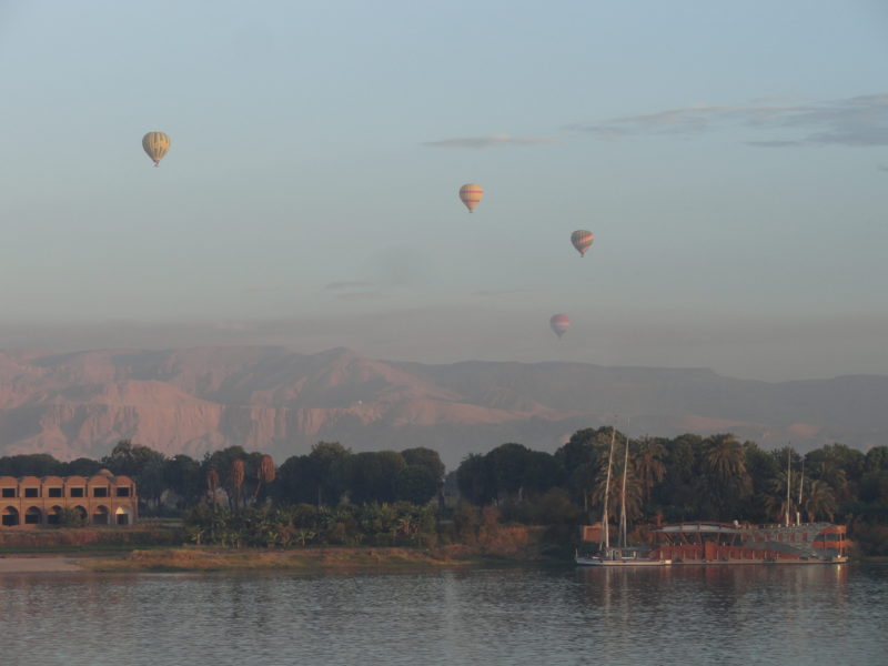 River with boat, mountains, and hot air balloons